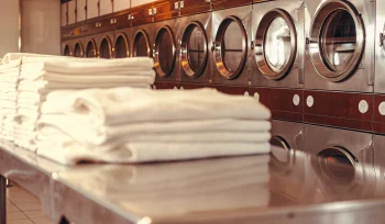 Stacks of clean healthcare linens in front of industrial washers at a Brookville laundry service.