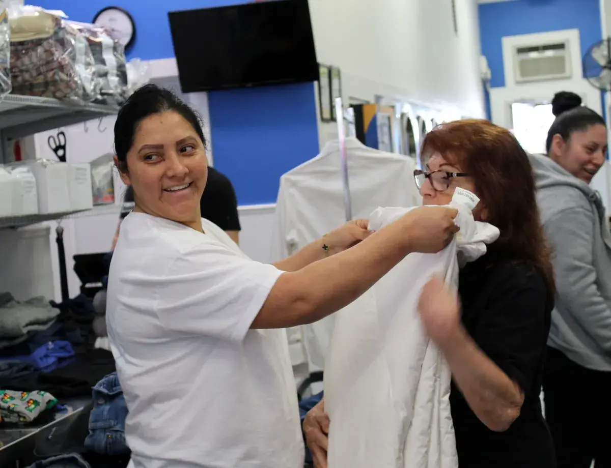 Two Long Island Laundry Company team members folding a white sheet together in Glen Cove