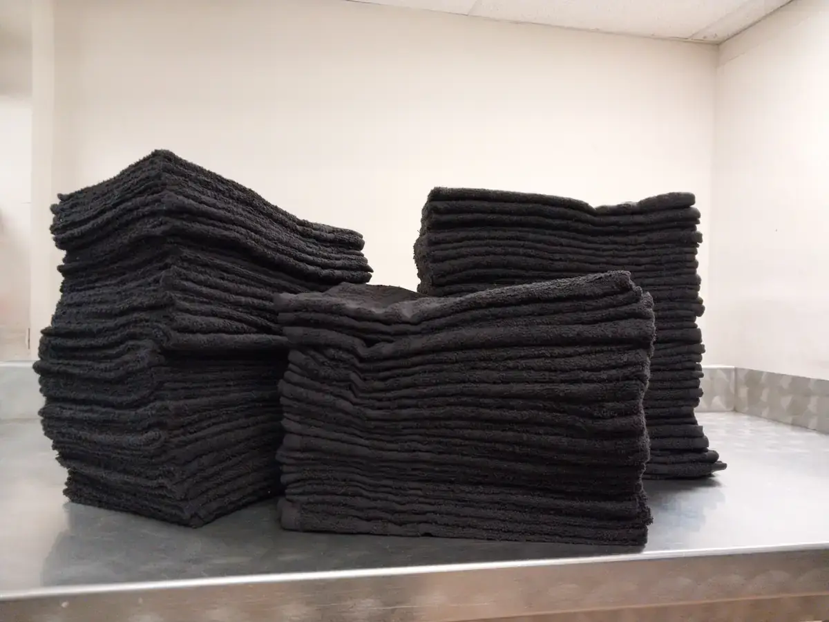 Stacks of folded black salon towels at Long Island Laundry Company in Glen Cove